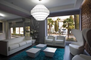 A modern living room with a sofa, two armchairs, and a coffee table. There is a large window with a view of palm trees and a building.