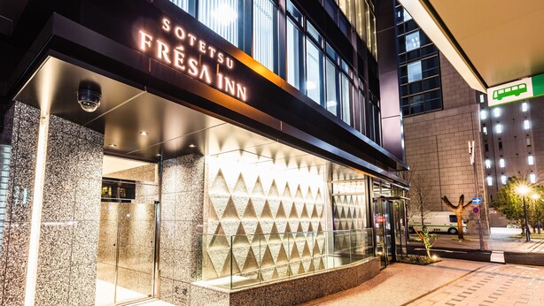 En hotelindgang med en moderne facade, en glasklagedør og et skilt, der siger "Sotetus Fresa Inn".