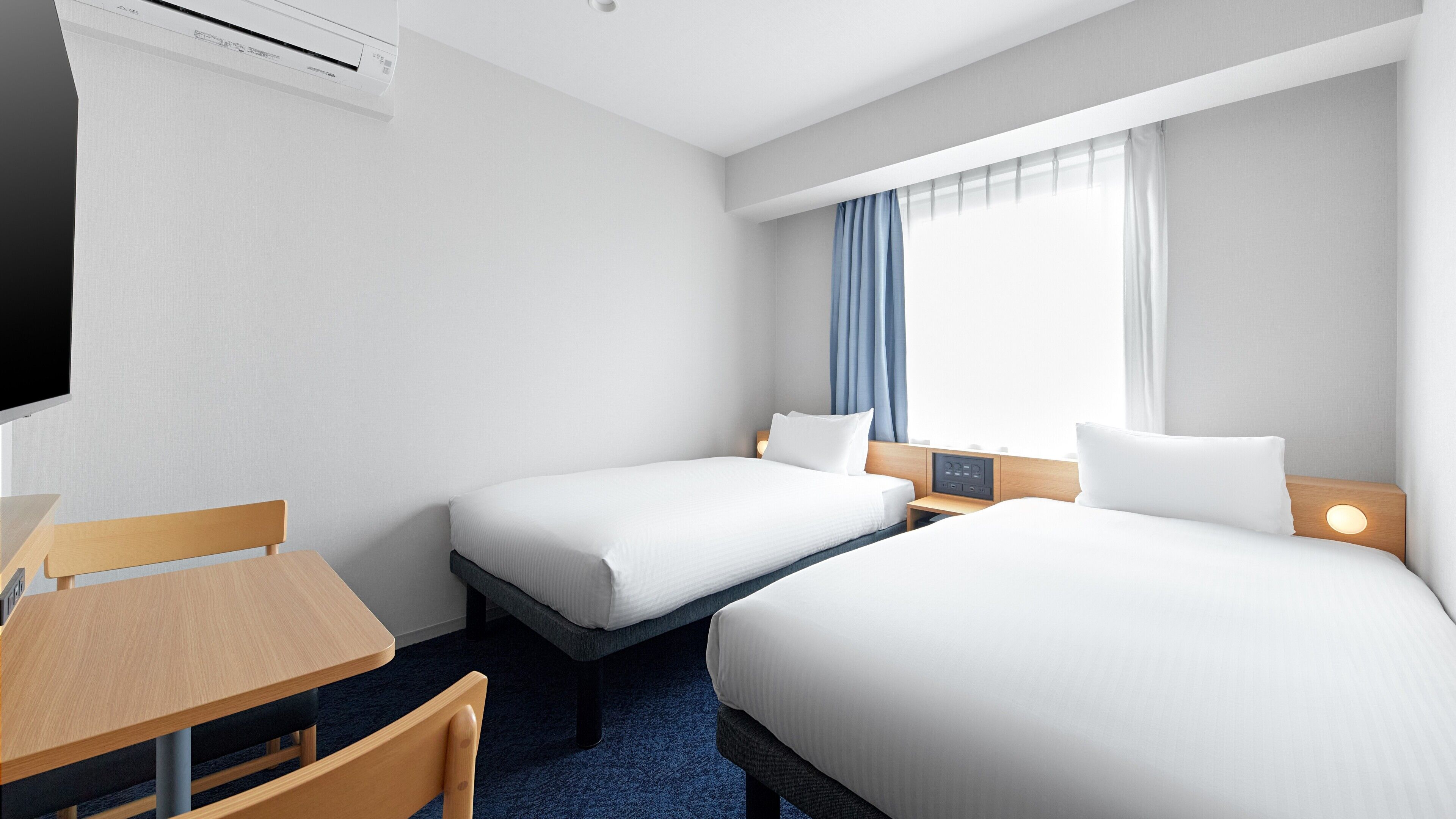 A hotel room with two beds, a desk, a chair, a TV, and a window with curtains.