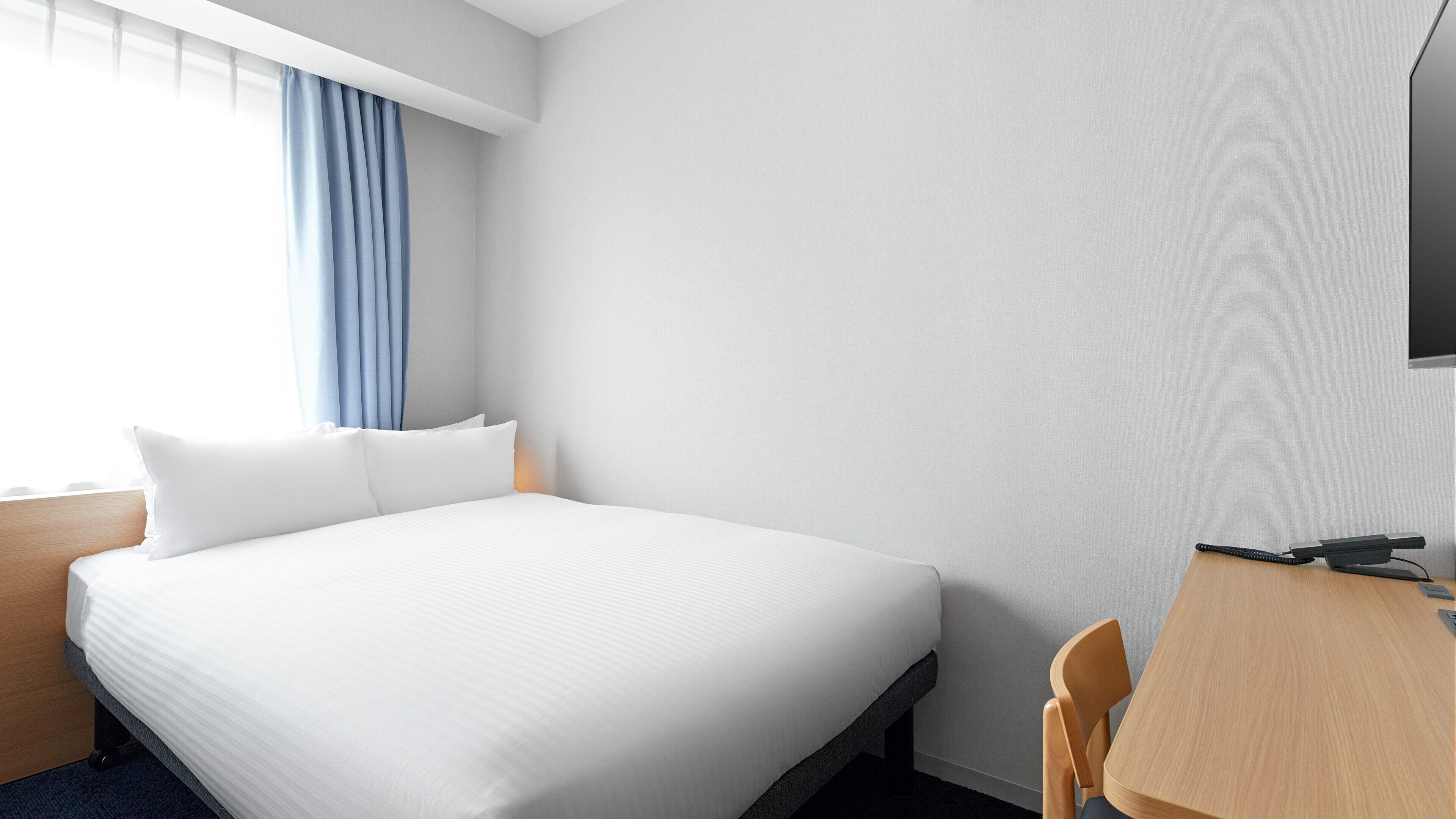 A hotel room with a bed, a desk, a chair, a TV, and a window with curtains.