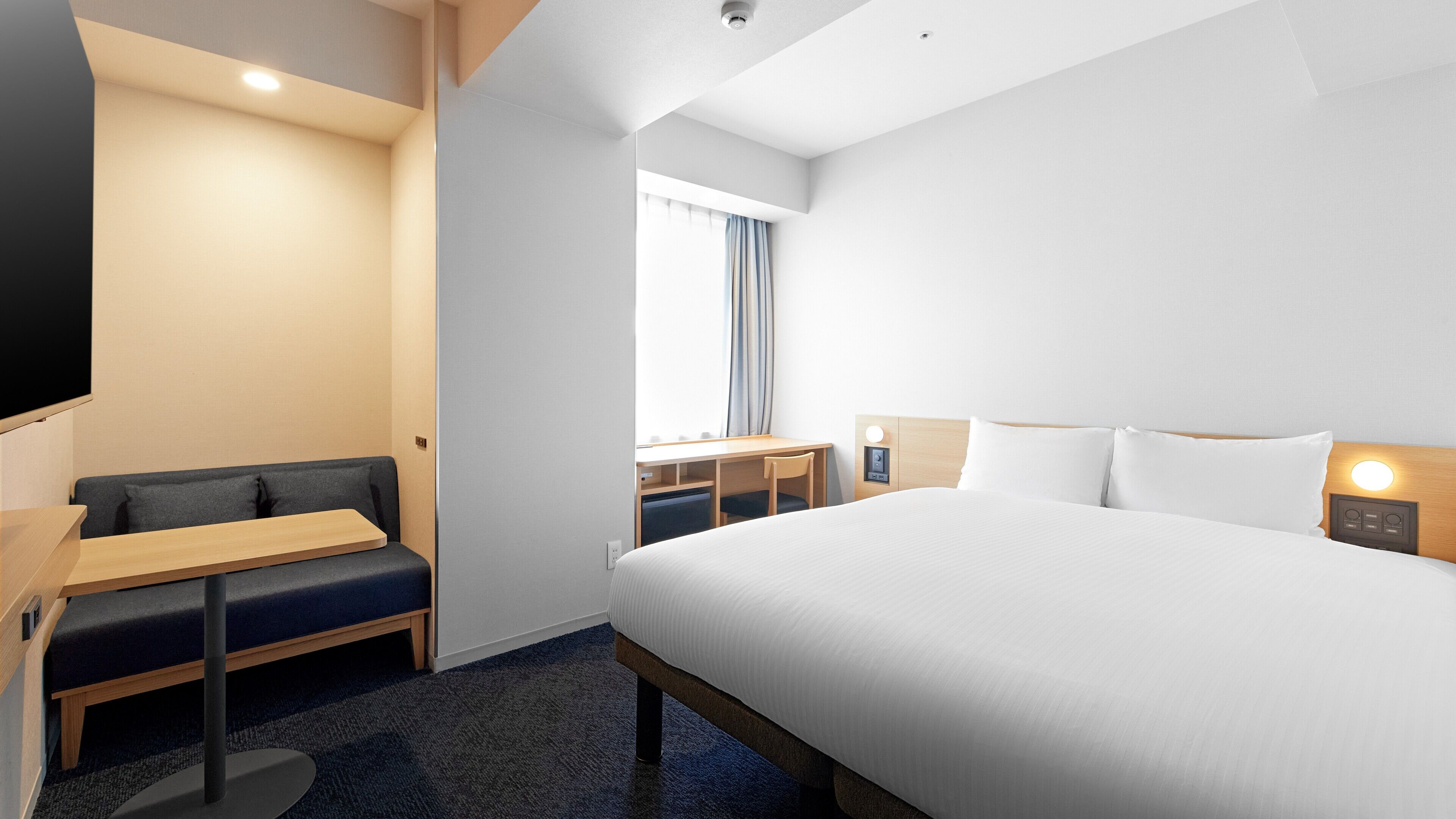 A hotel room with a bed, a desk, a chair, a sofa, and a TV.