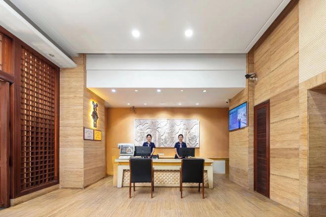 A reception area with a reception desk, two receptionists, a wall-mounted TV, and a decorative wall piece.