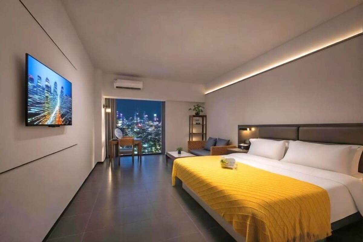 Een moderne hotelkamer met een groot bed, een televisie aan de muur, een balkon met uitzicht op de stad, en een klein zitje.