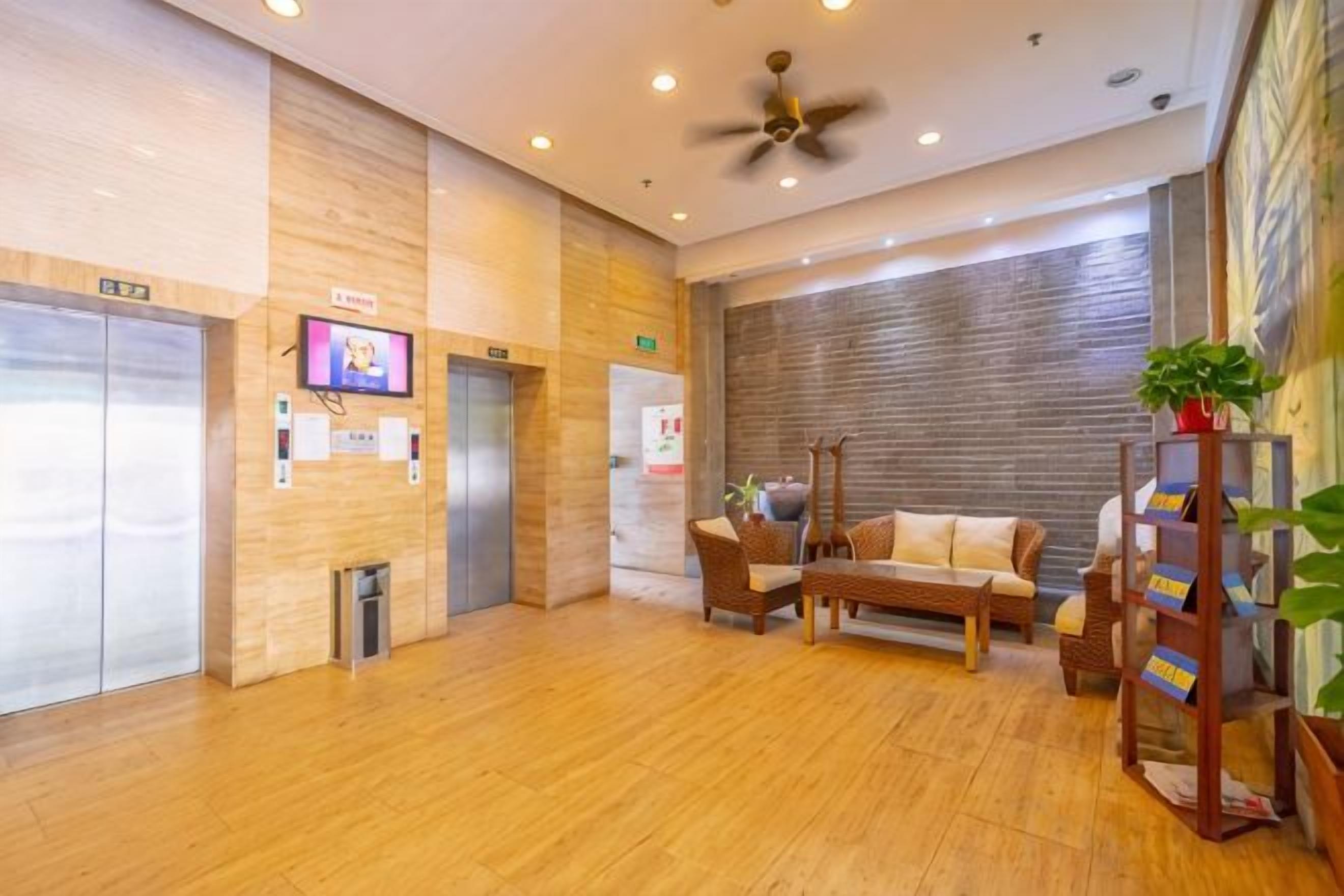 Una hall d'hotel con pavimento in legno, una ventola a soffitto, un divano, un tavolino da caffè e una libreria.