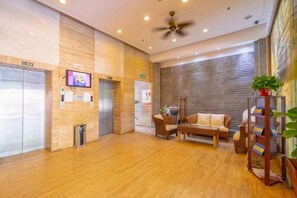 Un vestíbulo de hotel con suelo de madera, un ventilador de techo, un sofá, una mesa de centro y una estantería.