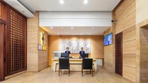 A reception area with two receptionists at a desk, wooden panel walls, and a large abstract artwork above the desk. - Shenlan Urban Hotel Apartment (Wanlvyuan Friendship Sunshine City Branch) (Haikou)