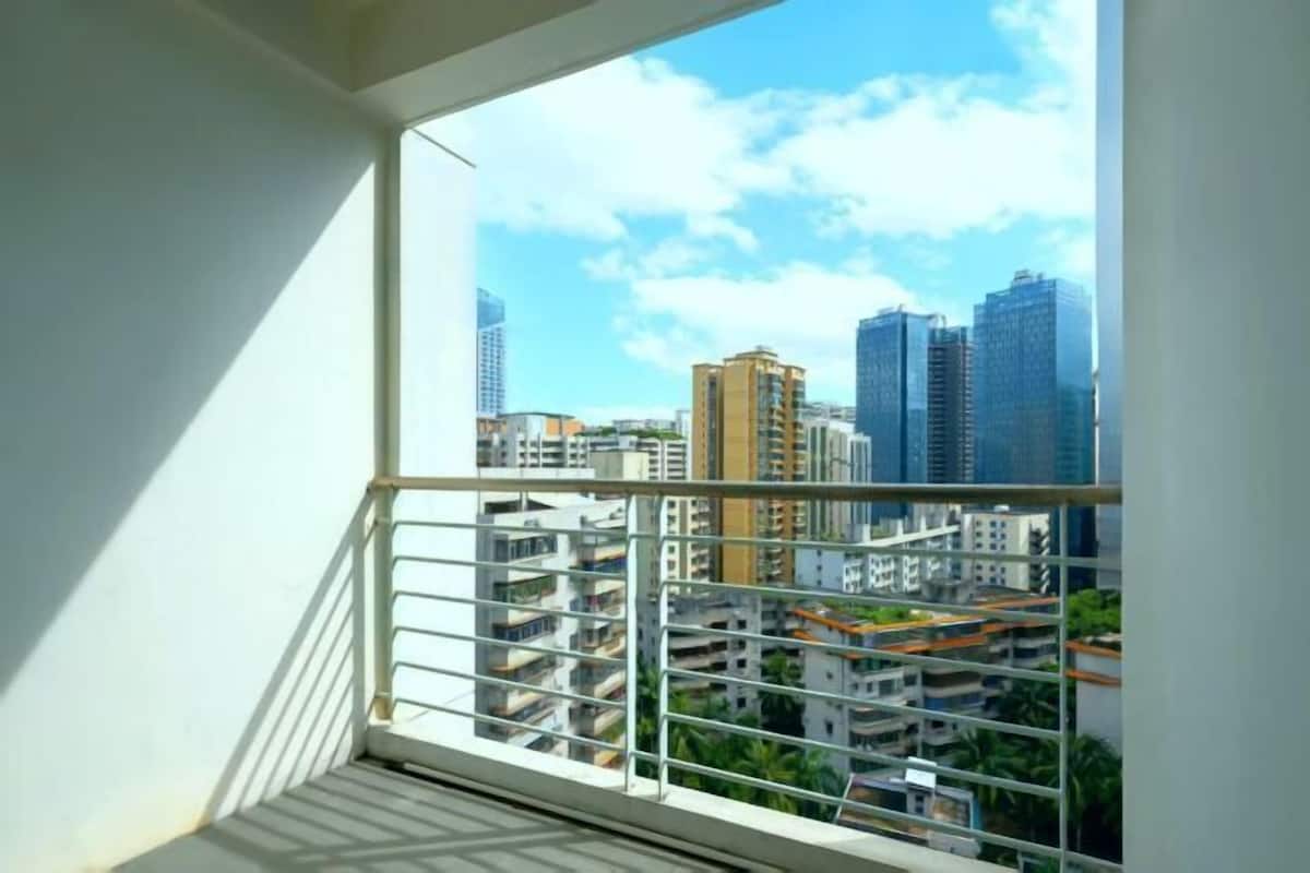Een balkon met uitzicht op de stad, een metalen hekwerk en een witte muur.