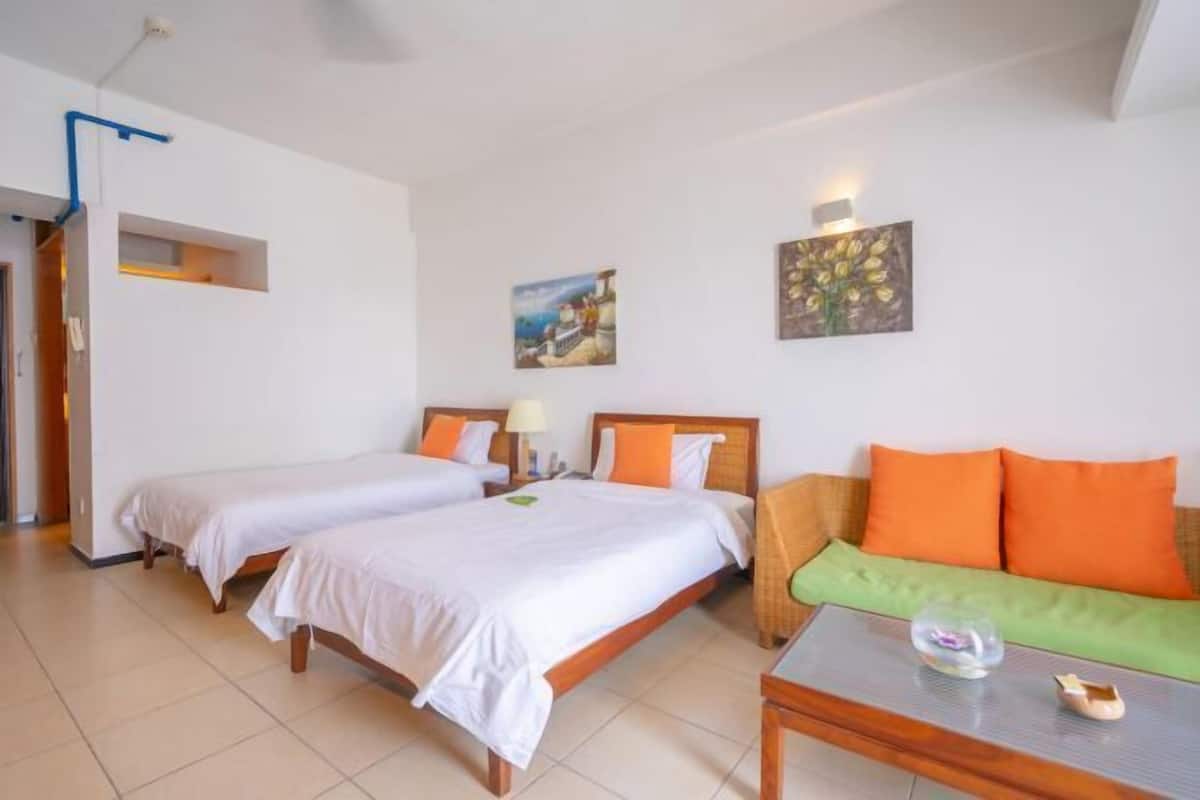 Een hotelkamer met twee eenpersoonsbedden, een slaapbank, een bijzettafeltje en kunstwerken aan de muren.