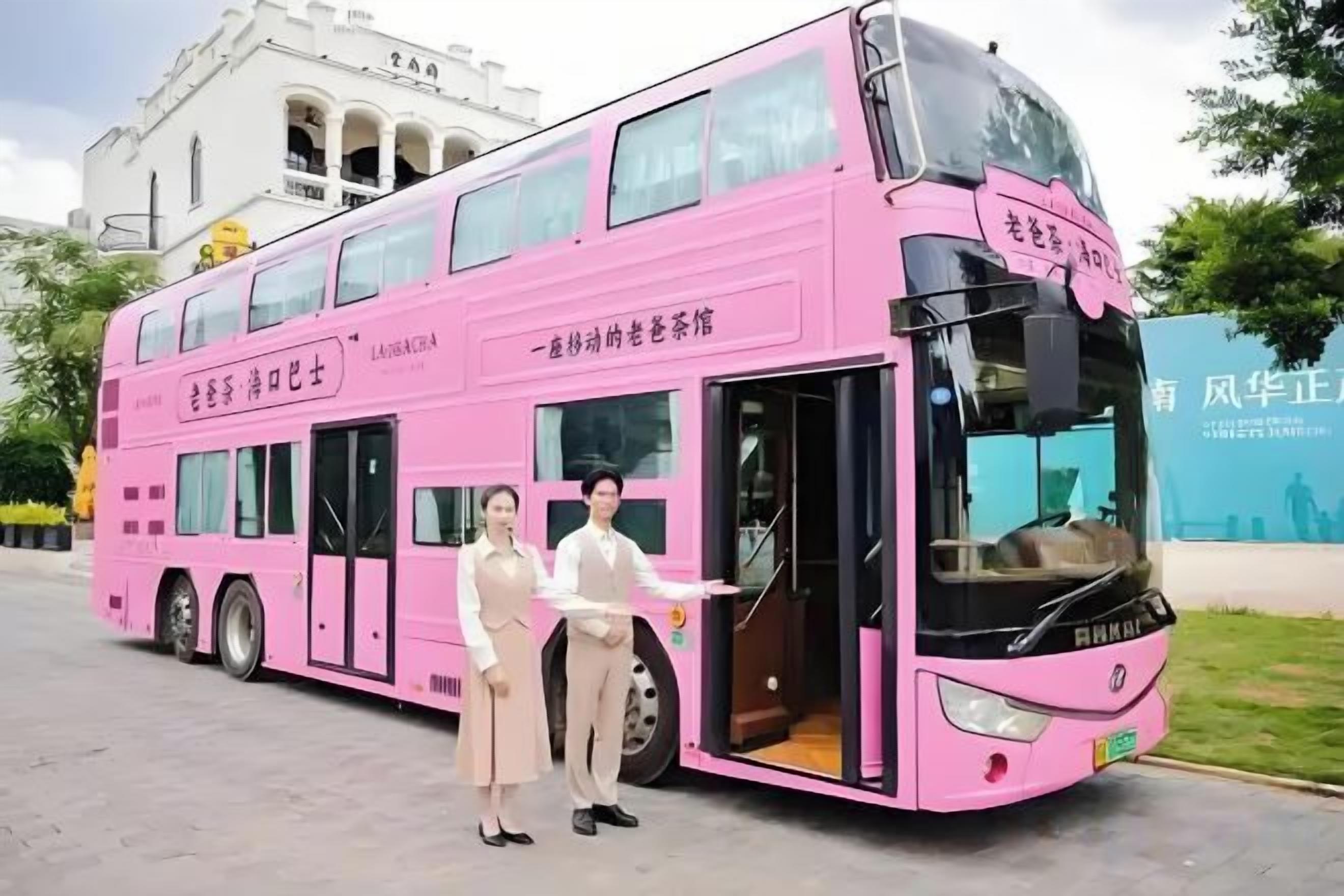 A pink double-decker bus with a driver and a passenger standing at the front.