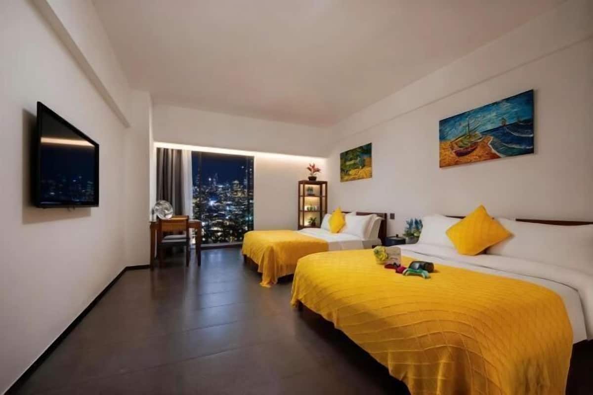 Hotelkamer met twee bedden, een televisie, kunst aan de muur en uitzicht op de stad 's nachts.