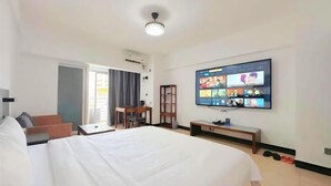 A hotel room with a large bed, a desk, a chair, a TV mounted on the wall, and a window with curtains. - Shenlan Urban Hotel Apartment (Wanlvyuan Friendship Sunshine City Branch) (Haikou)