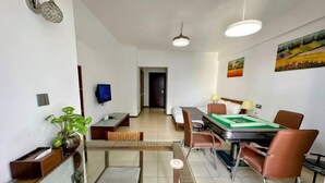 A modern dining area with a glass table, brown chairs, and a green tablecloth. There is a television on the wall and a door in the background. - Shenlan Urban Hotel Apartment (Wanlvyuan Friendship Sunshine City Branch) (Haikou)