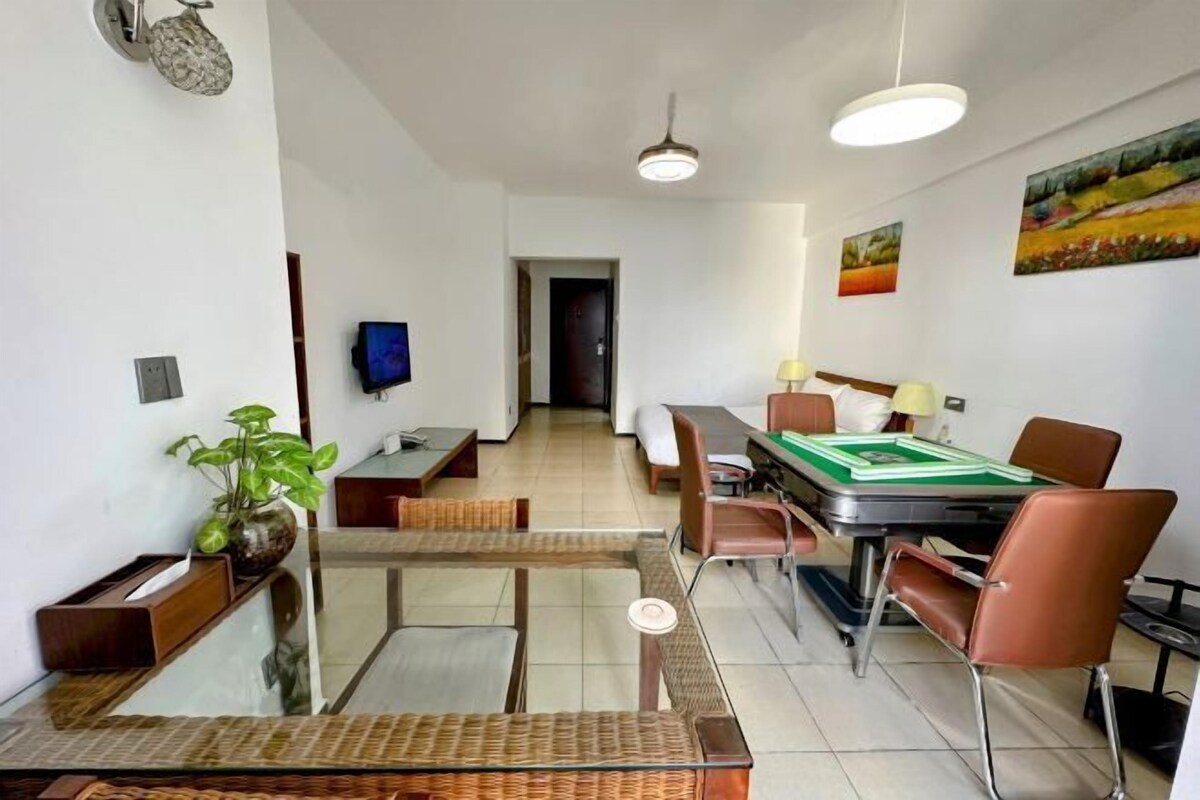 A modern dining area with a glass table, brown chairs, and a green tablecloth. There is a television on the wall and a door in the background.