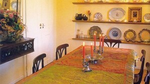 A dining room with a long table, chairs, a chandelier, and wall-mounted shelves with plates and decorative items. - Casa Do Castelo (Peniche)