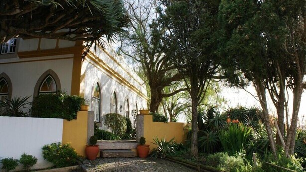 A building with arched windows and a yellow facade, surrounded by lush greenery and trees. - Casa Do Castelo (Peniche)