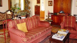 A living room with a red sofa, a coffee table with magazines, a mirror, and a wooden cabinet. - Casa Do Castelo (Peniche)