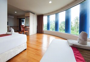 Een hotelkamer met twee bedden, een houten vloer, een groot raam met uitzicht en een klein bureau met stoel.