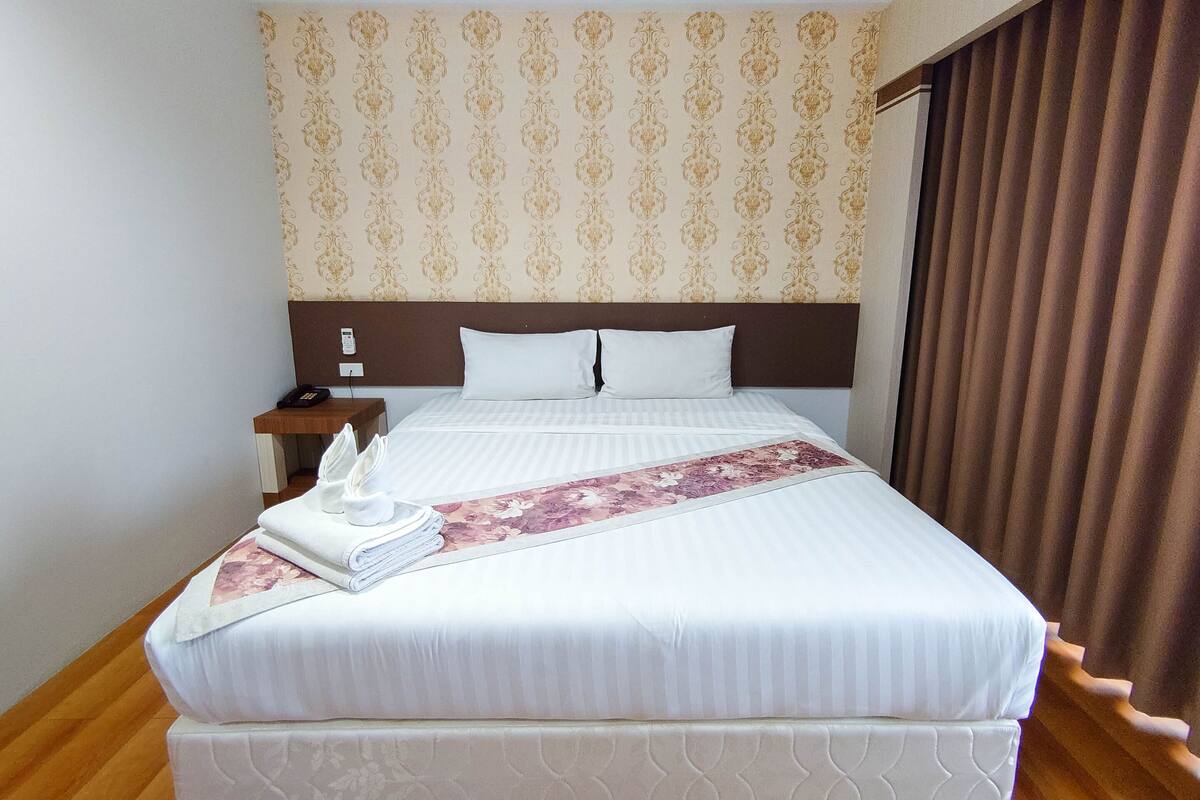 Una cama bien hecha con un corredor floral, una mesita de noche de madera con una lámpara y un papel tapiz estampado.