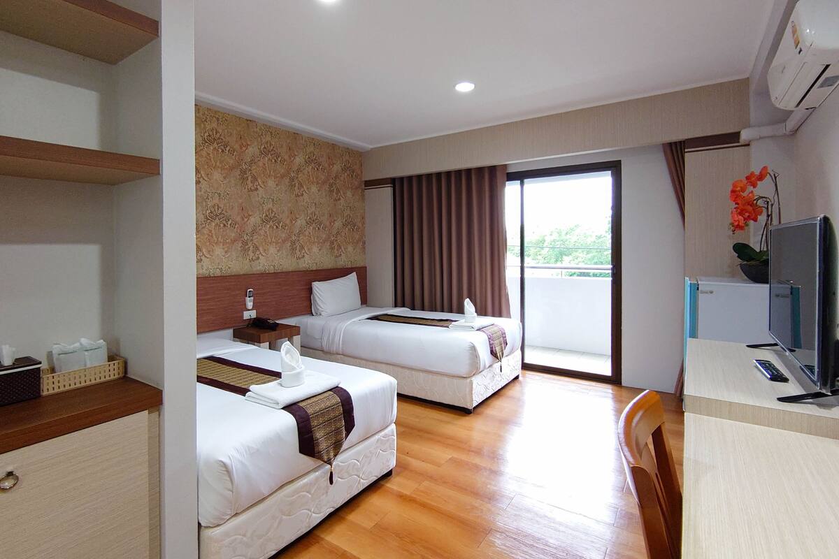 Habitación de hotel con dos camas, un escritorio con computadora y televisión.