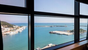 A coastal view through a window with a clear sky, a harbor with boats, and a distant shoreline with buildings. - Hotel The Club Yeonhwari (Busan)
