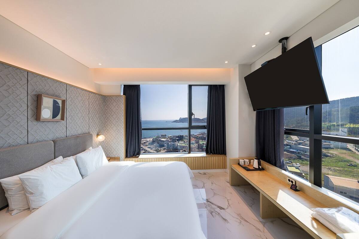 A hotel room with a large bed, a desk, a flat-screen TV, and a city view.