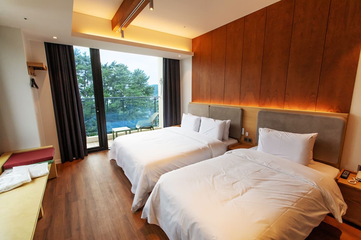 A hotel room with two beds, wooden flooring, a balcony with a view, and a small seating area.
