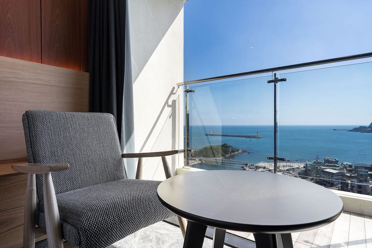 A balcony with a view of the sea, a chair, and a table.
