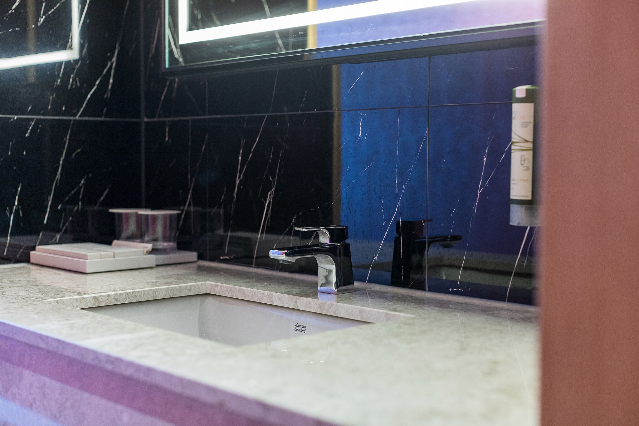 A bathroom with a modern sink, a mirror, and a blue tiled wall.