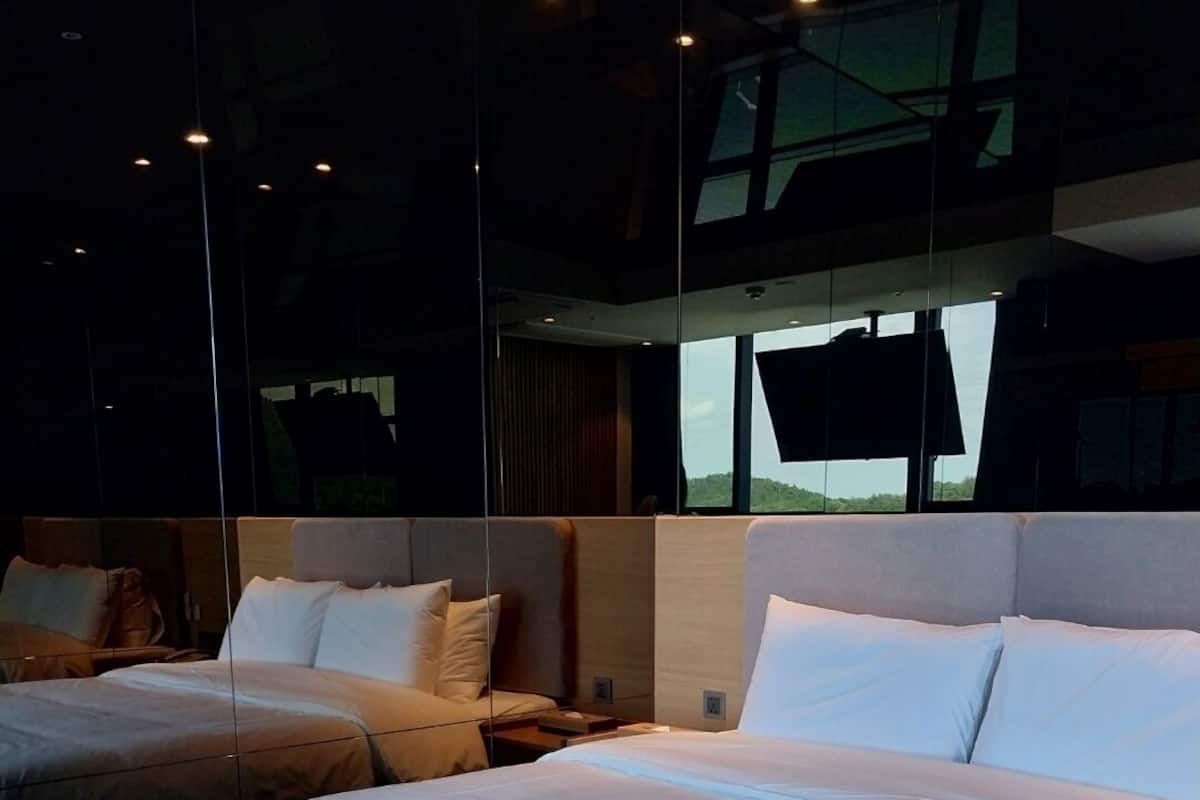 A modern hotel room with two beds, a large mirror, and a view of the outdoors.