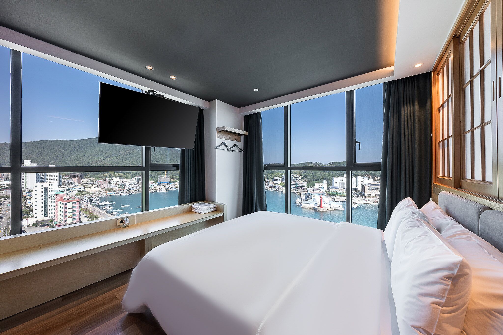 Habitación de hotel con una cama grande, un televisor montado en la pared y vistas a un paisaje urbano y al agua.