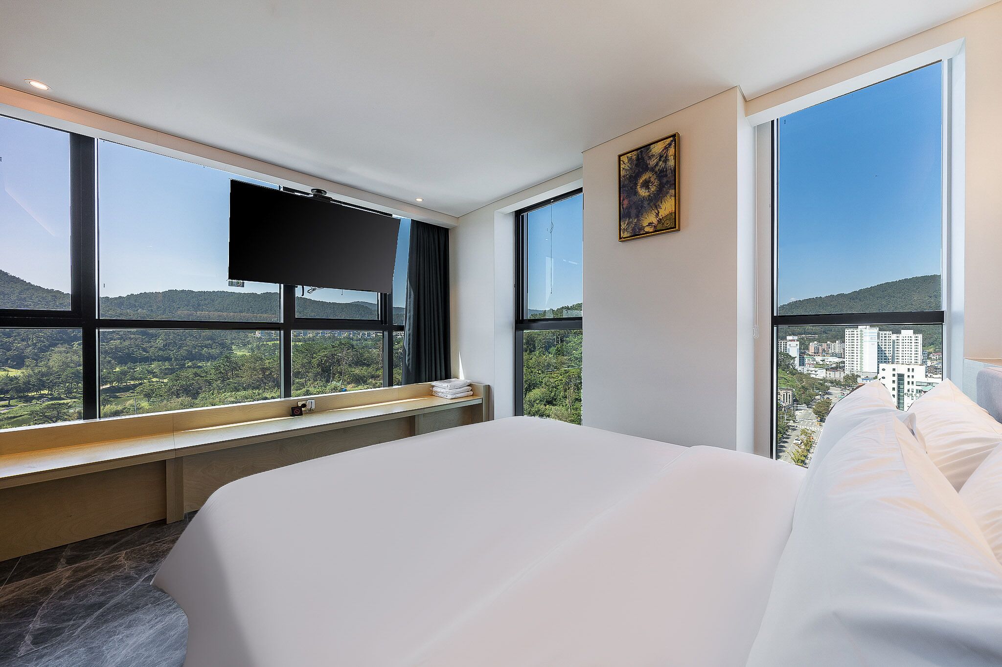 A hotel room with a large bed, a flat-screen TV, and a city view through large windows.