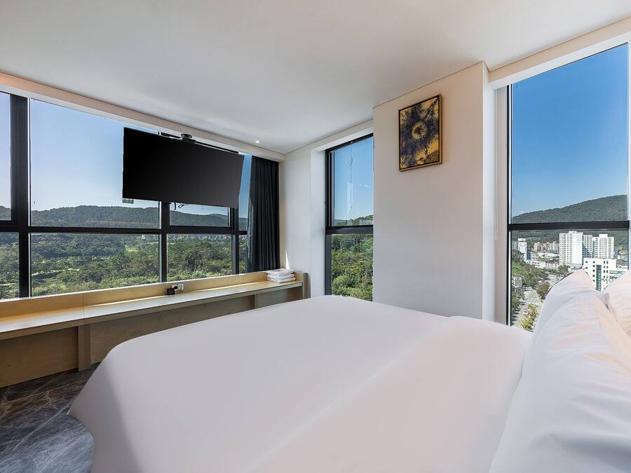 A hotel room with a large bed, a flat-screen TV, and a city view through large windows.