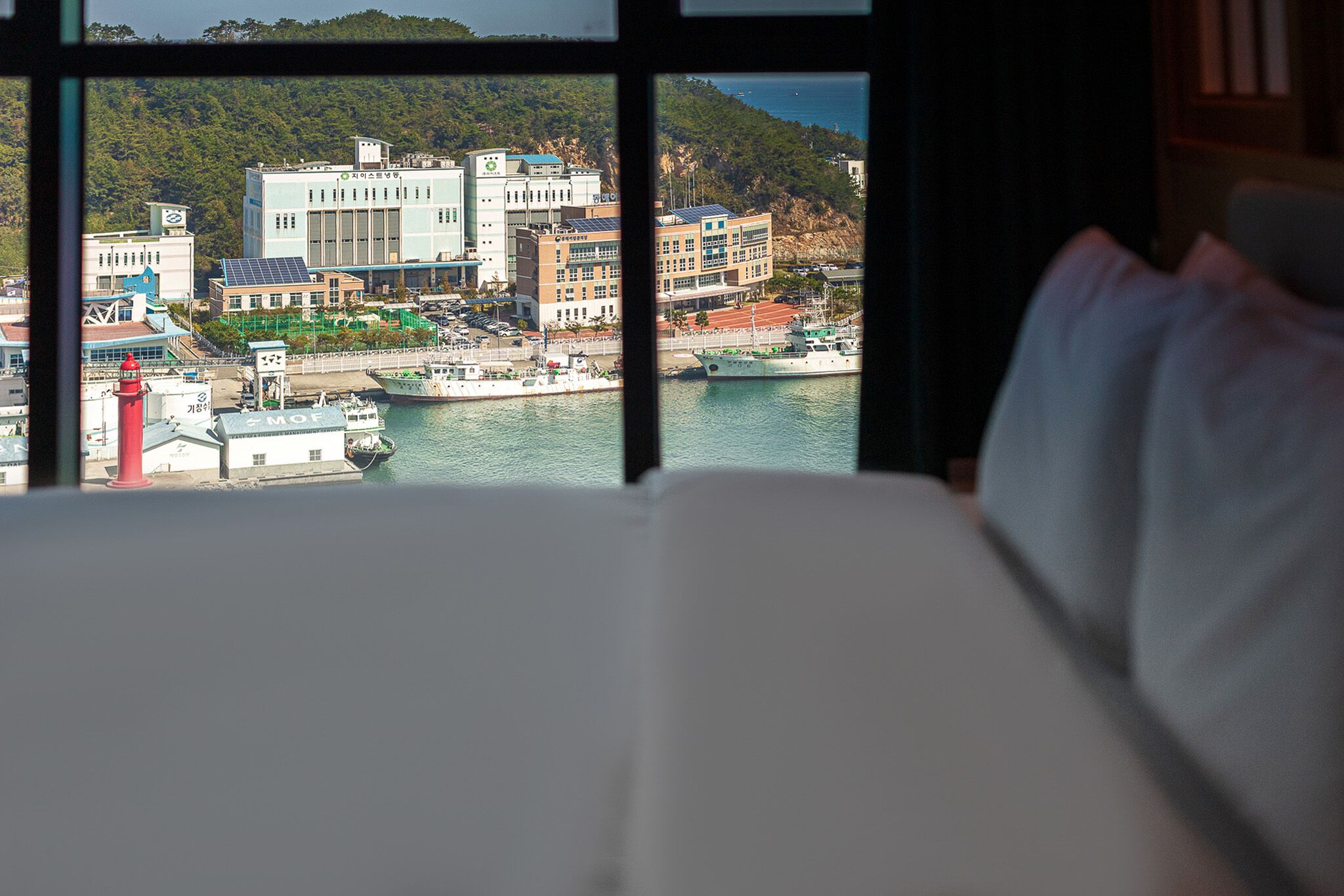 A hotel room with a view of a coastal town, including buildings, a lighthouse, and boats.