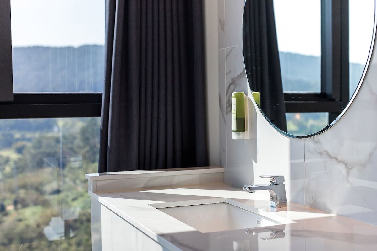 A bathroom with a large window, a mirror, and a sink.