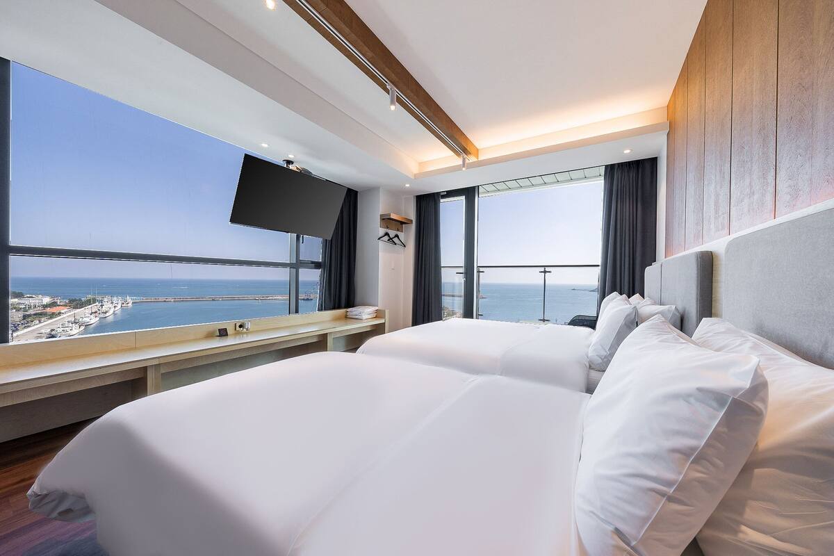 A hotel room with a large bed, a TV mounted on the wall, and a view of the sea.
