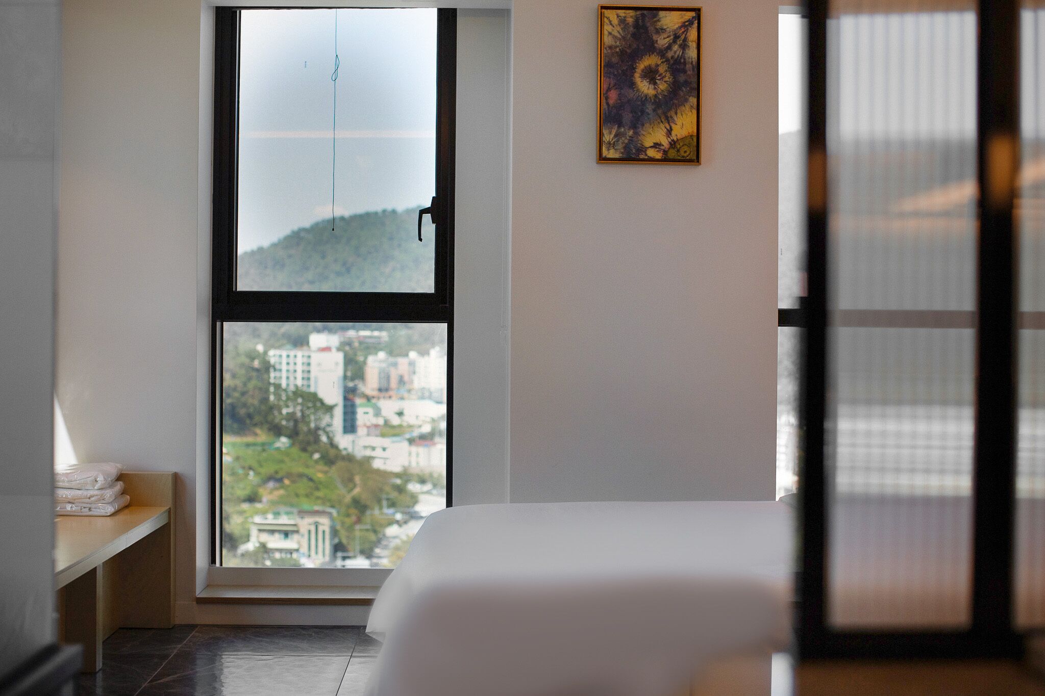 A hotel room with a large window, a bed, a bedside table with towels, and a framed picture on the wall.