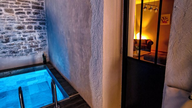 Een wellnessruimte met een stenen muur, een houten vloer en een glazen deur naar een ruimte met een brandende lamp.
