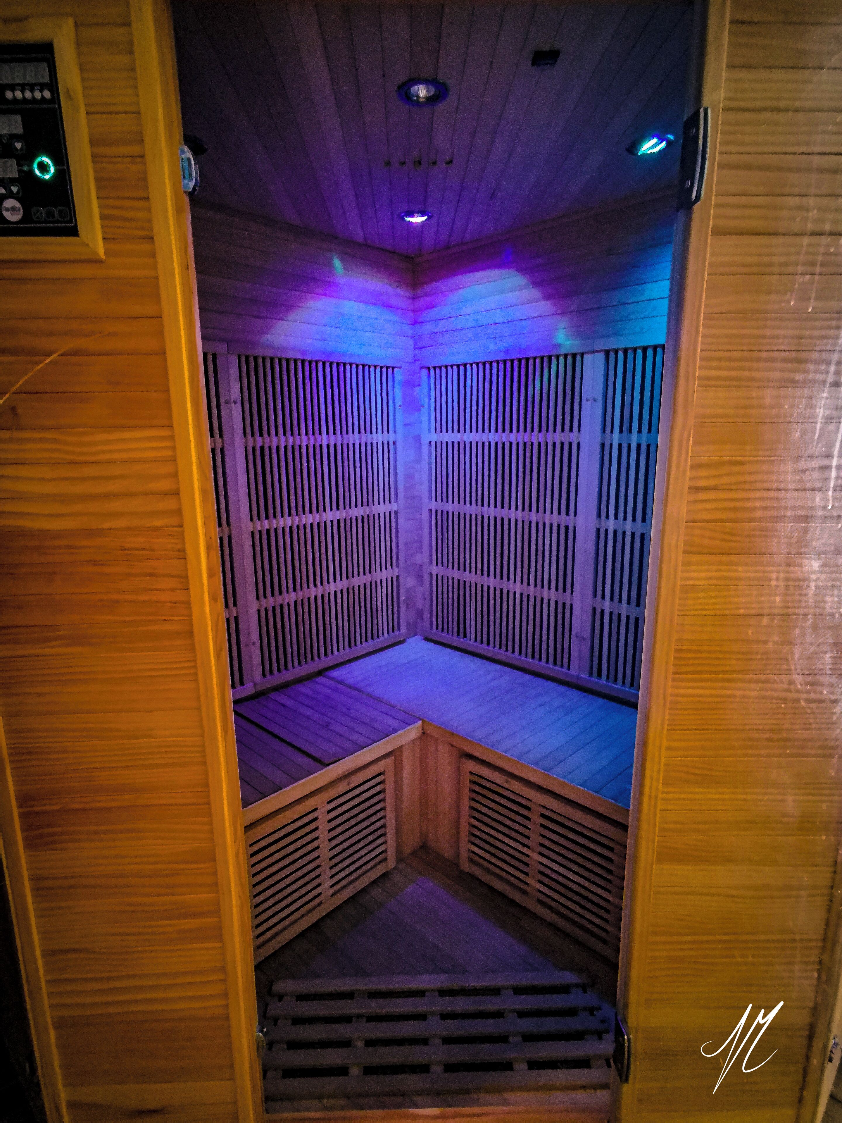 Een sauna met houten wanden en een schuine kap, voorzien van een bedieningspaneel en ventilatieroosters.