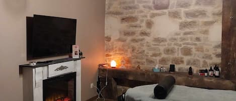 Una habitación acogedora con pared de piedra, chimenea, televisor y cama.