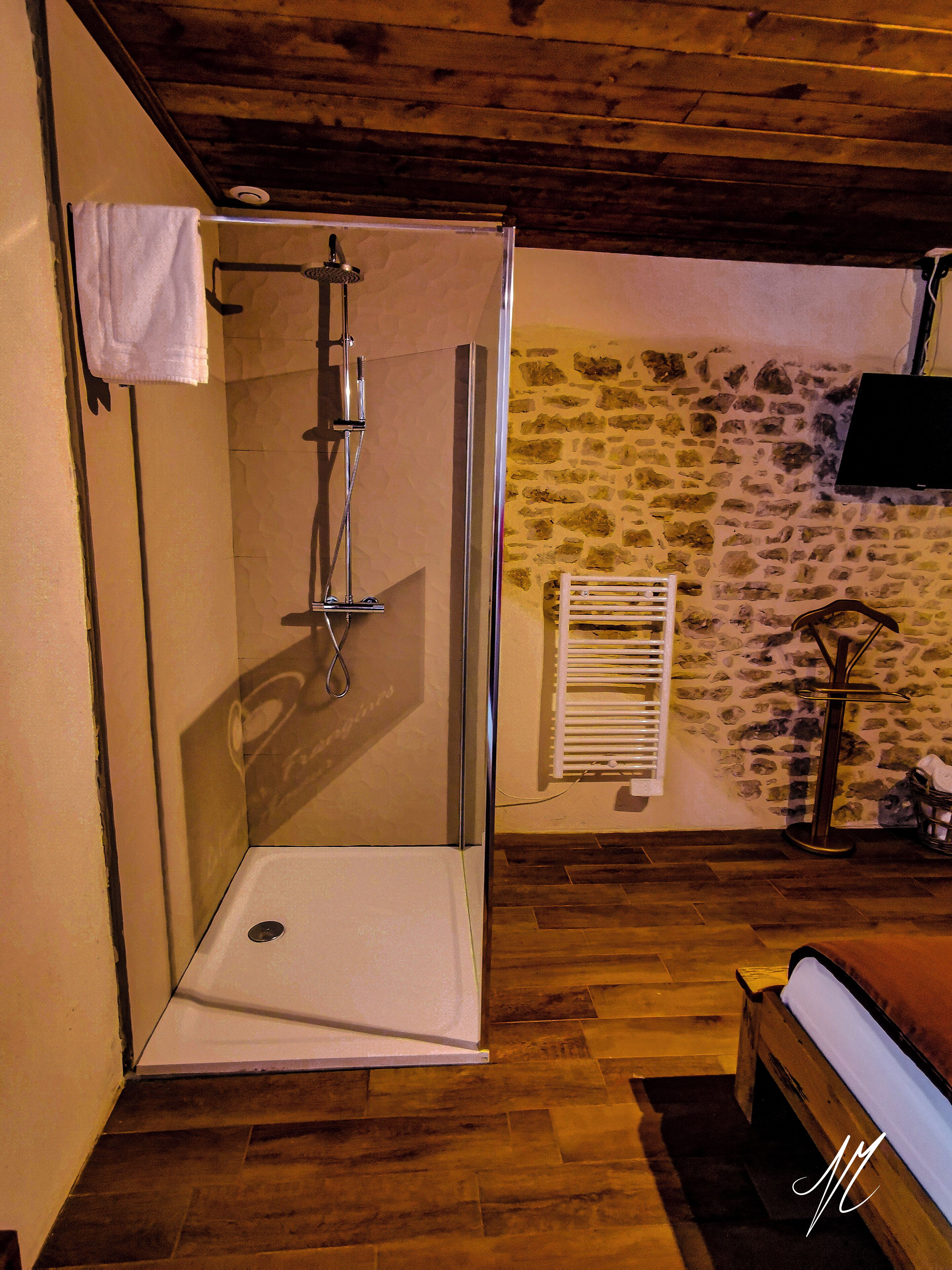 A shower with a glass door, a stone wall, and a bed with a wooden headboard.