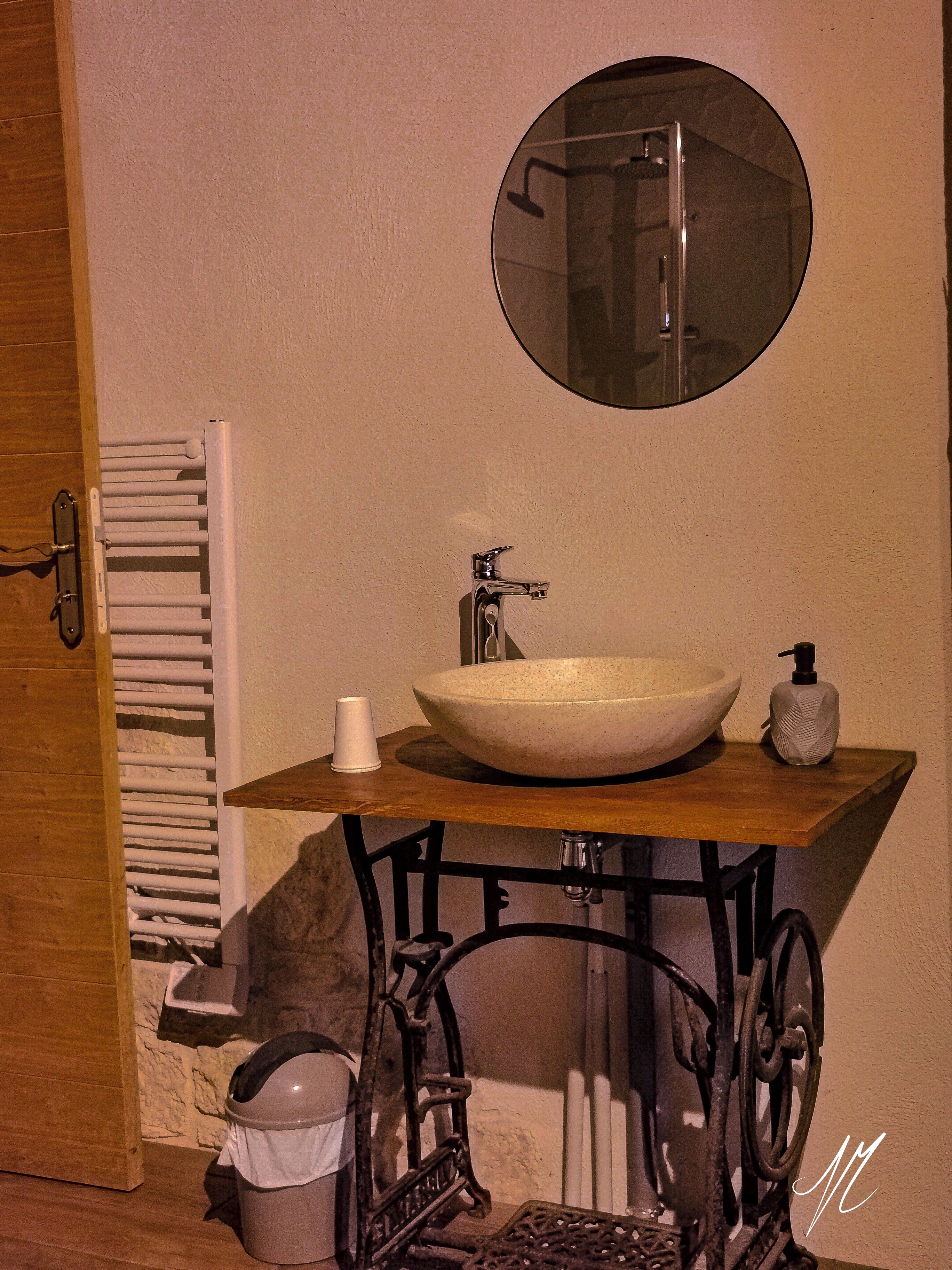 A bathroom with a wooden vanity, a round mirror, a white sink, and a towel rack.