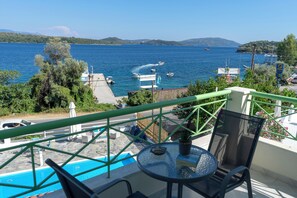 A balcony with a pool, chairs, and a table overlooking a body of water with boats. - Tropicana Inn (Lefkada)