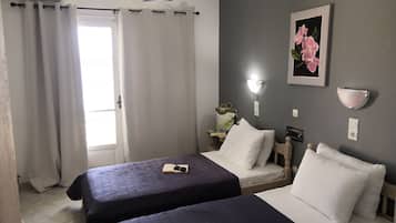 Hotellihuone, jossa on kaksi sänkyä, yöpöytä lampun kanssa, seinään kiinnitetty valaisin ja kehystetty taulu.
