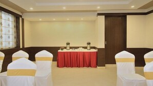 Un salón de conferencias con una mesa roja, sillas blancas con cintas doradas y una puerta de madera.