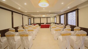 Un salón de conferencias con filas de sillas, un escenario con una mesa roja y amplias ventanas con vidrio emplomado.