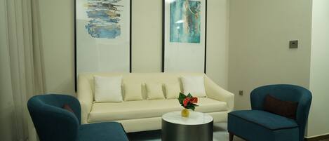 A modern living room with a sofa, two armchairs, a coffee table, and abstract art on the wall.