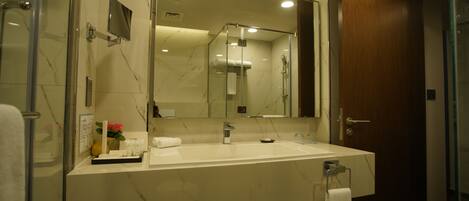 A modern bathroom with a large mirror, a white sink, and a glass-enclosed shower.