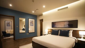 Una habitación de hotel moderna con una cama grande, dos mesitas de noche, un tocador, un espejo y obras de arte en las paredes.