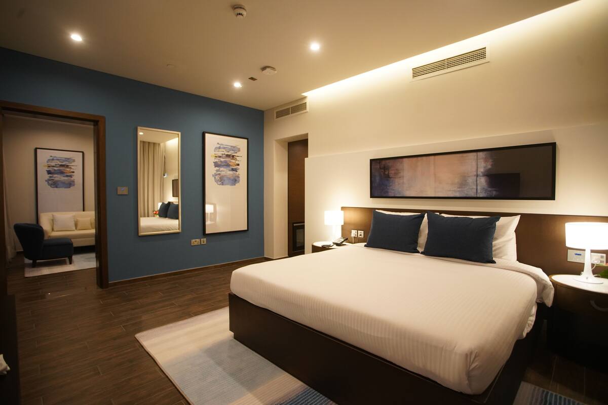 A modern hotel room with a large bed, two bedside tables, a nightstand, a mirror, and artwork on the walls.