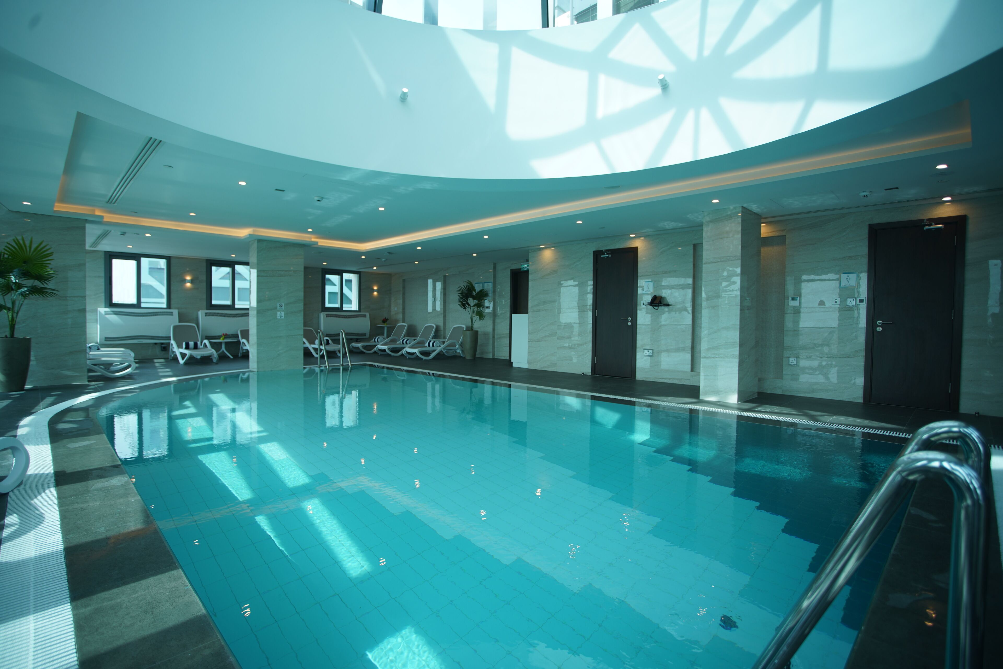 A large indoor swimming pool with clear water, surrounded by lounge chairs and a modern interior design.